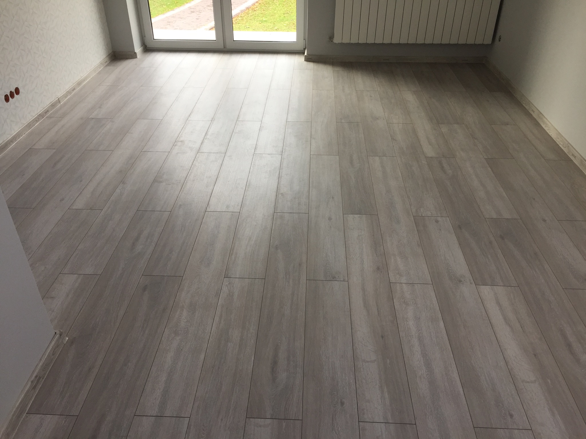 Ułożona podłoga z paneli imitujących drewno w jasnym, nowym pokoju z oknem balkonowym i grzejnikiem.