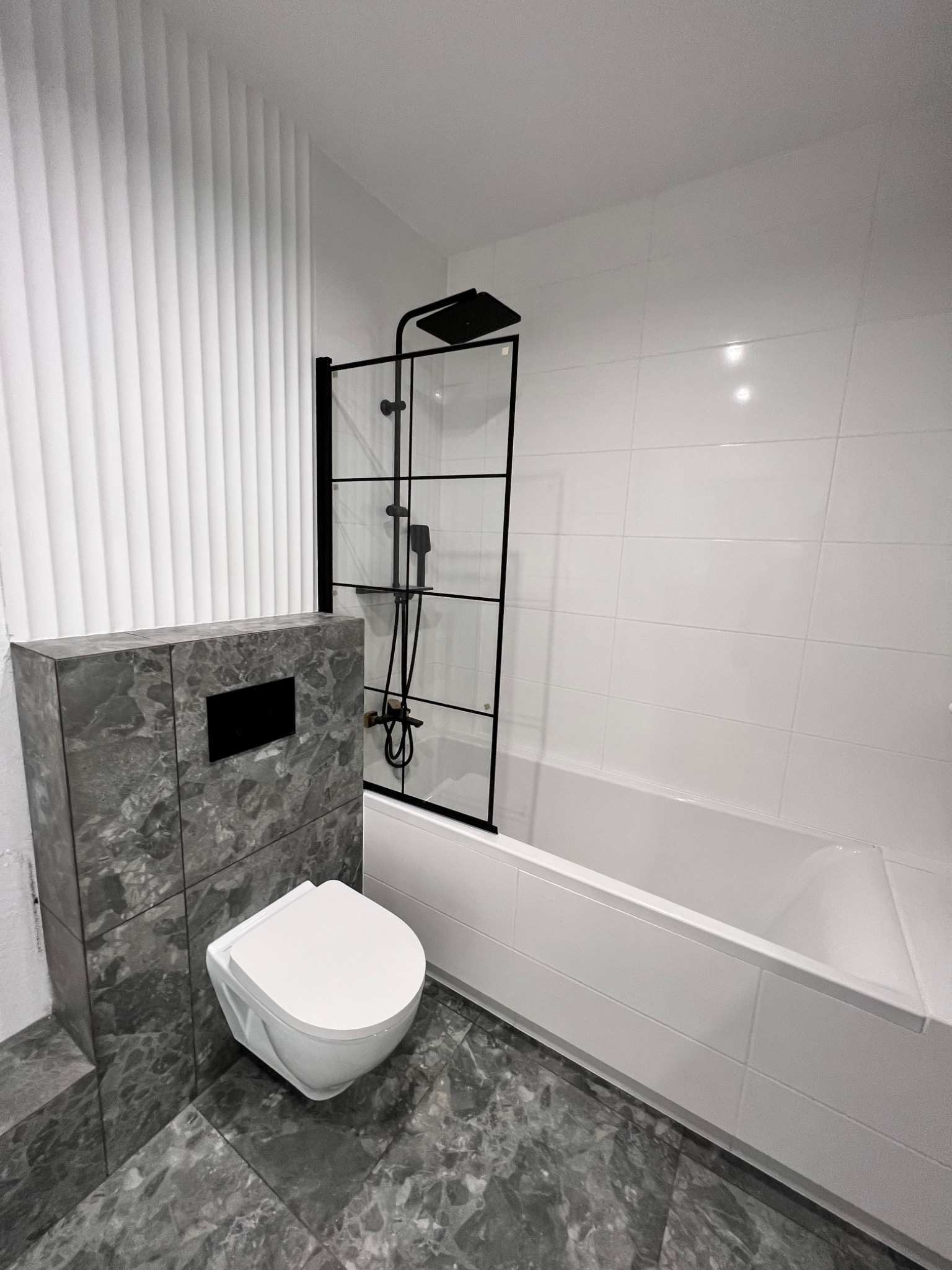 Nowoczesna łazienka z białą armaturą, szarą marmurową posadzką i kabiną prysznicową z czarnymi ramami.