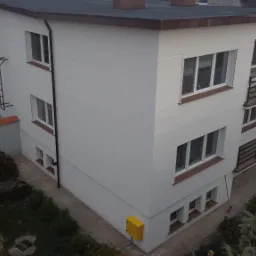 Trzypiętrowy budynek po renowacji elewacji, widoczna drabina przeciwpożarowa, balkony z czarną balustradą i żółta skrzynka gazowa na ścianie.