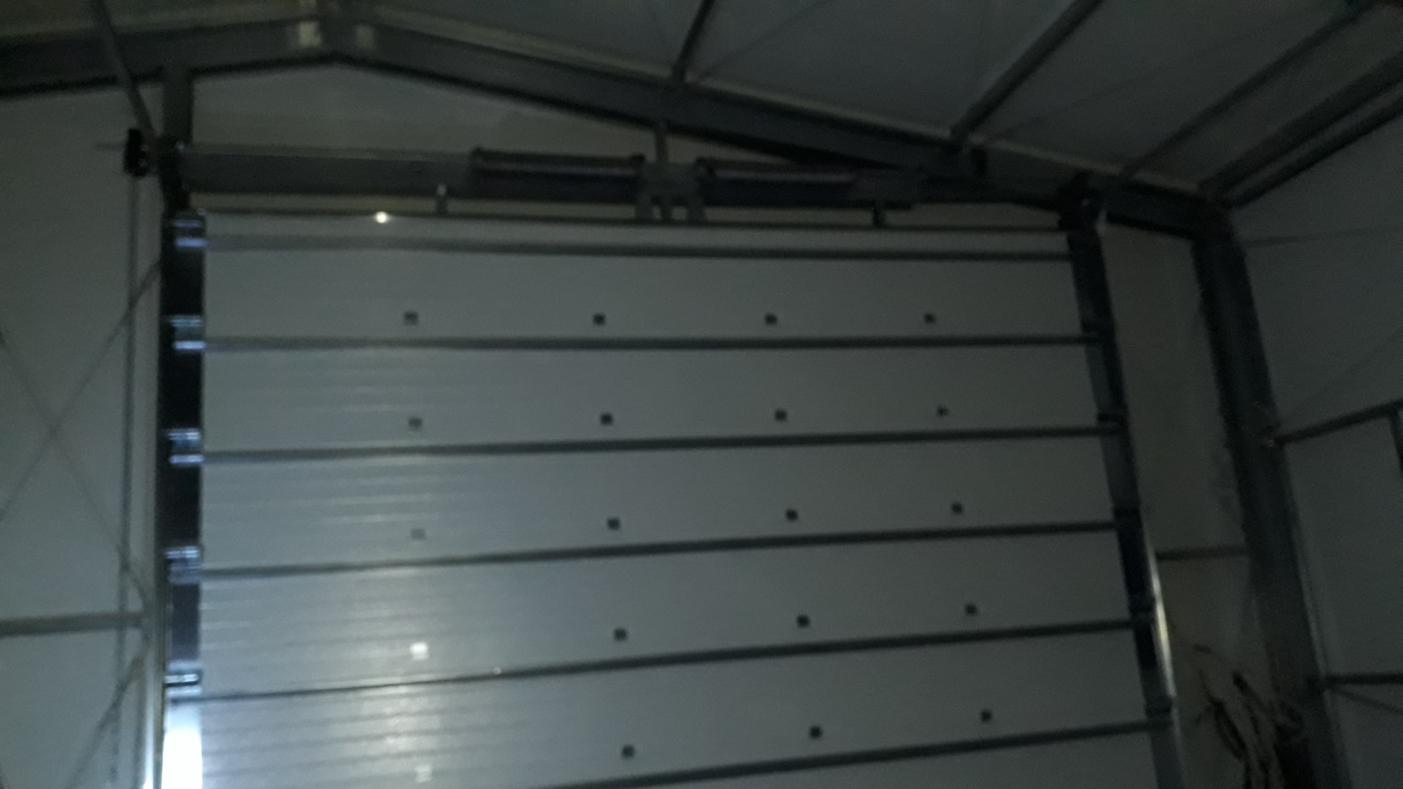 Zamknięta, segmentowa brama garażowa wewnątrz metalowej konstrukcji hali, widoczne prowadnice i mechanizm podnoszenia.