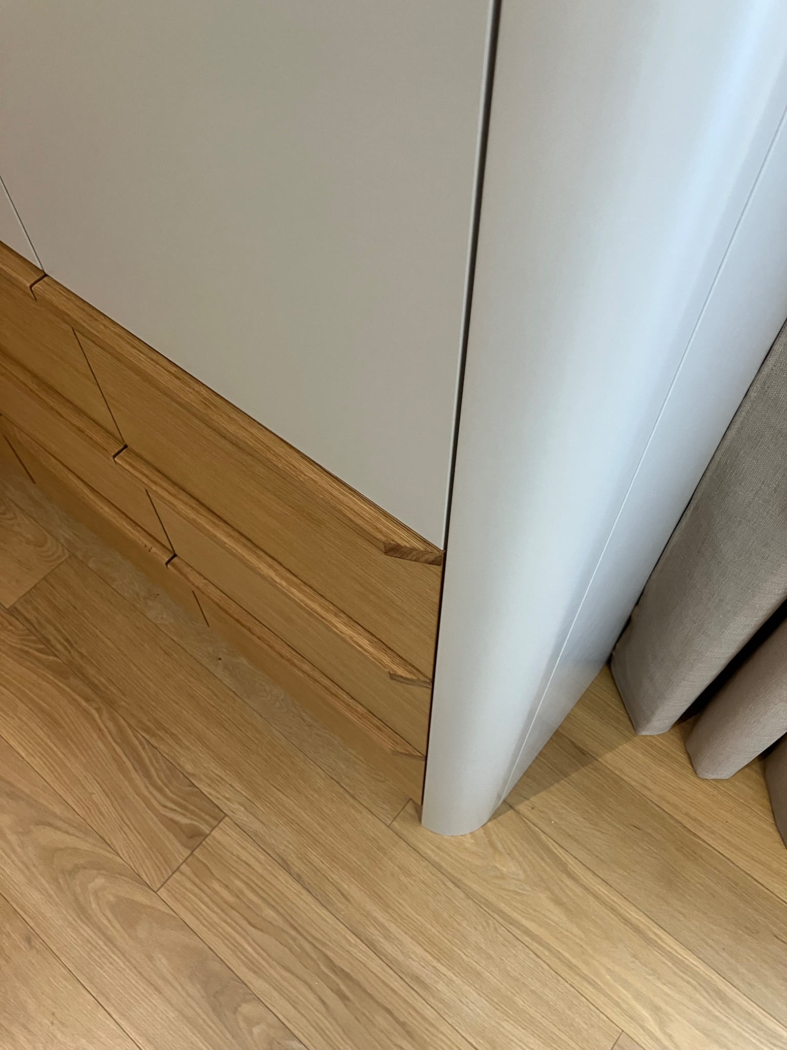 Fragment szafy z drewnianymi szufladami i białymi frontami, widok z góry, ukazujący detale wykończenia i strukturę drewna na podłodze.