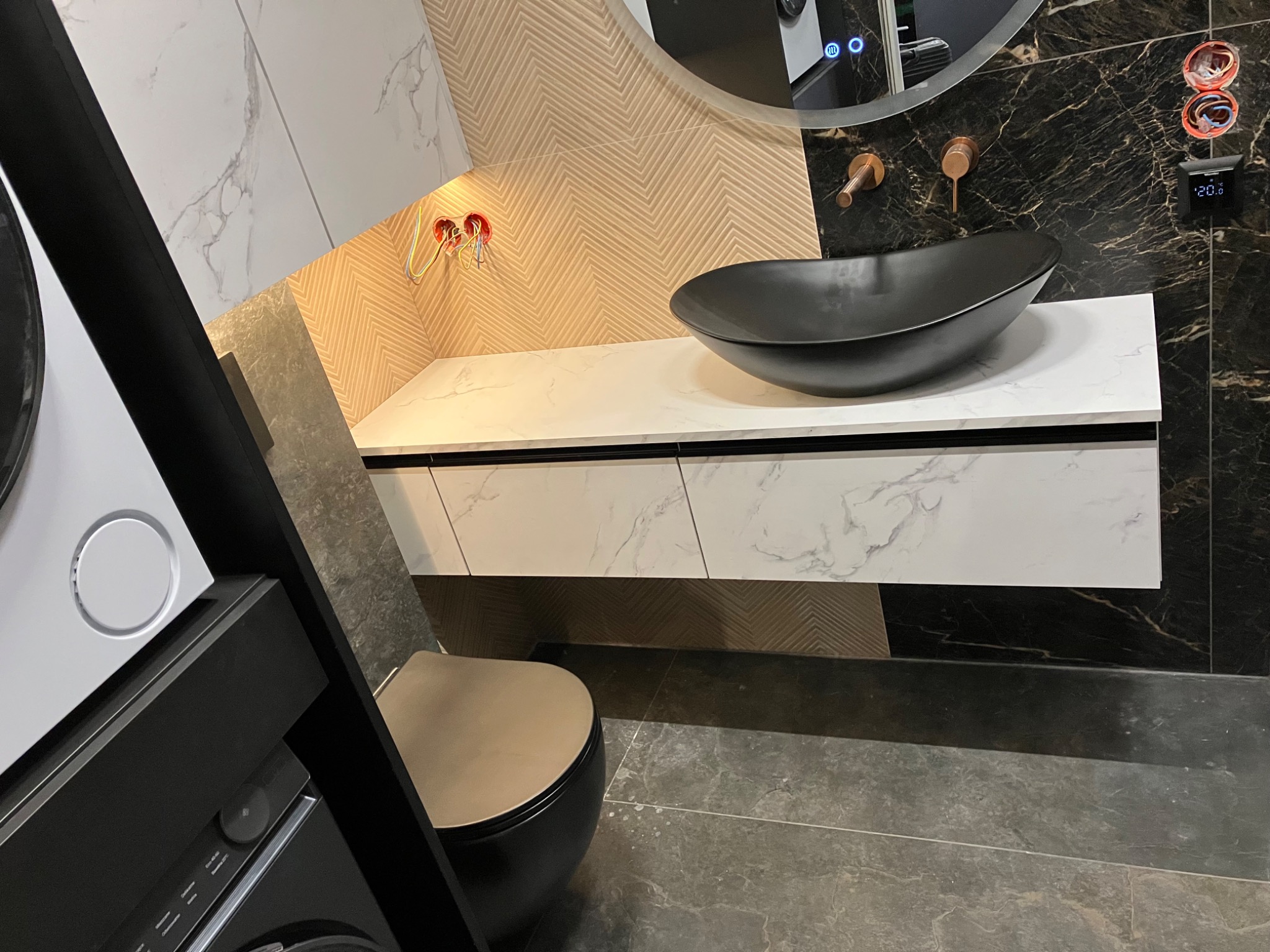 Nowoczesna łazienka z umywalką nablatową w kolorze czarnym, biały blat z marmurowym wzorem i szafka pod umywalką. Widoczne elementy instalacji elektrycznej.