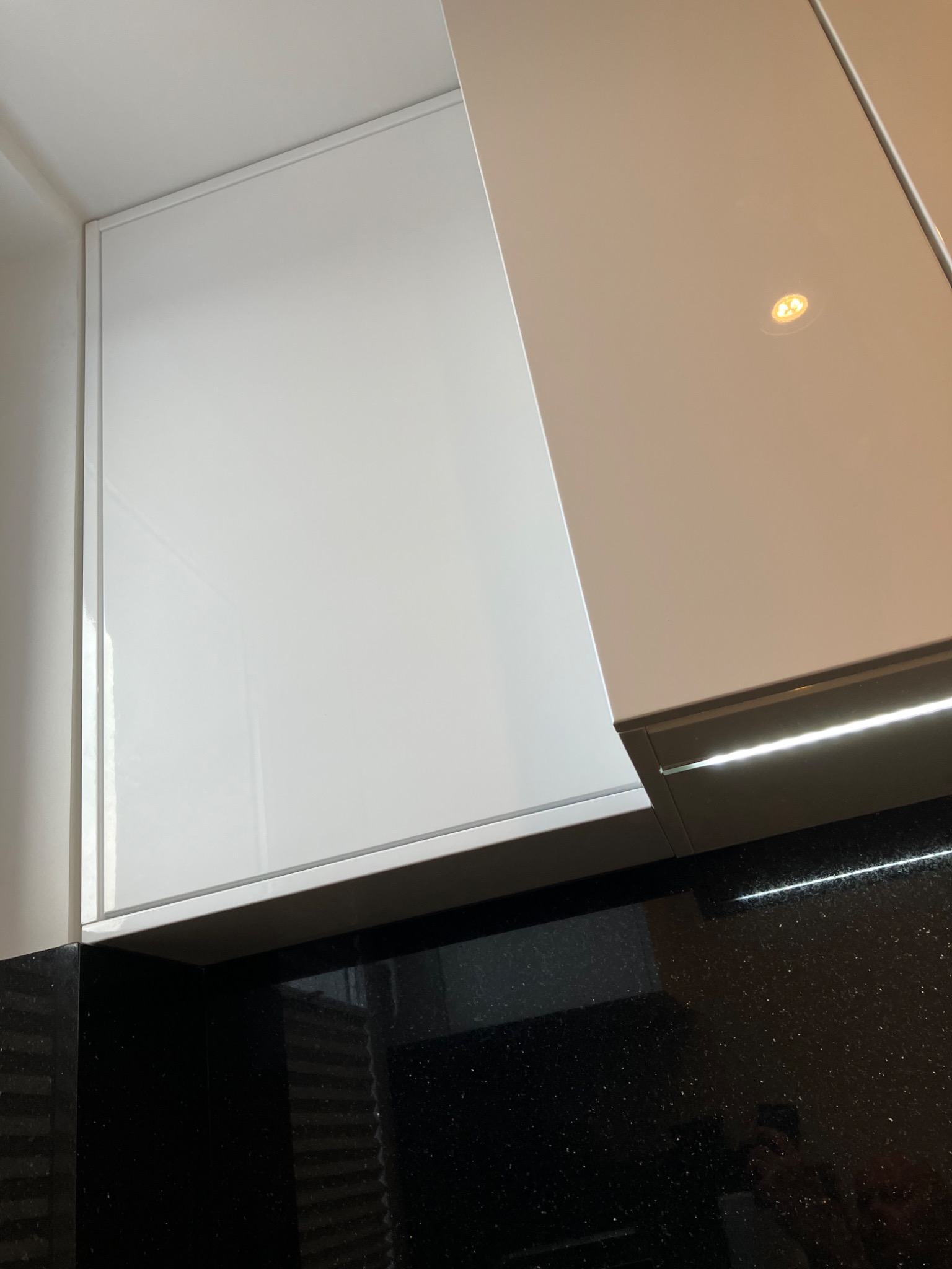 Białe, lakierowane fronty szafek kuchennych z oświetleniem LED podszafkowym i czarnym blatem z połyskiem. Minimalistyczny design.