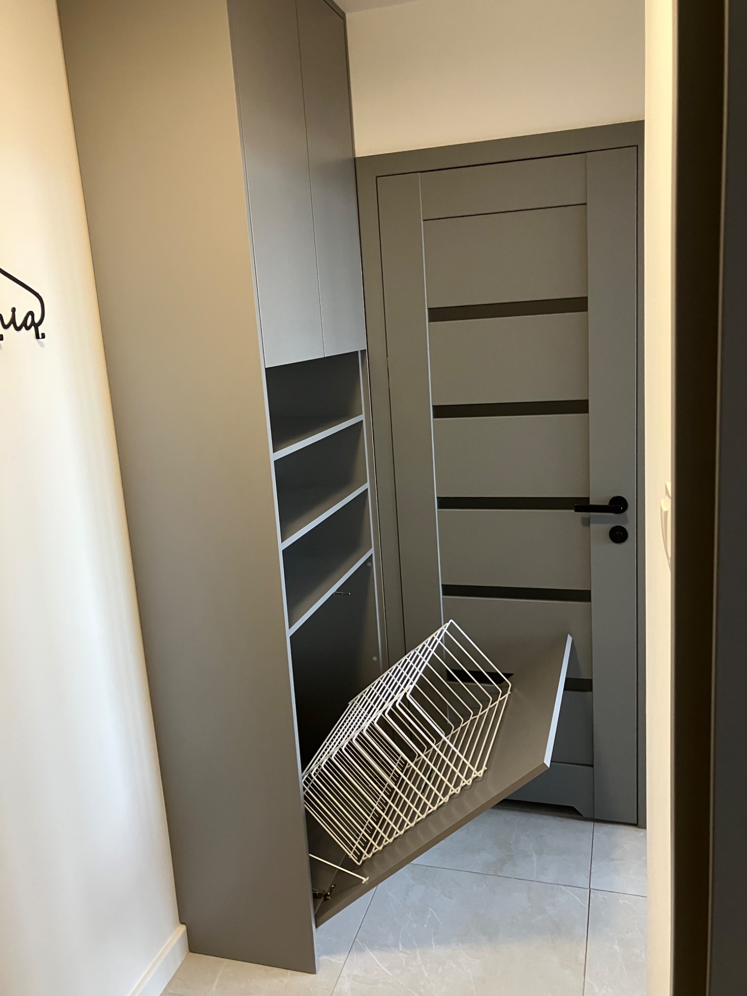 Szafa z wysuwanym koszem na buty, dopasowana do koloru drzwi, w mieszkaniu w Warszawie. Funkcjonalne rozwiązanie do przechowywania obuwia w przedpokoju.