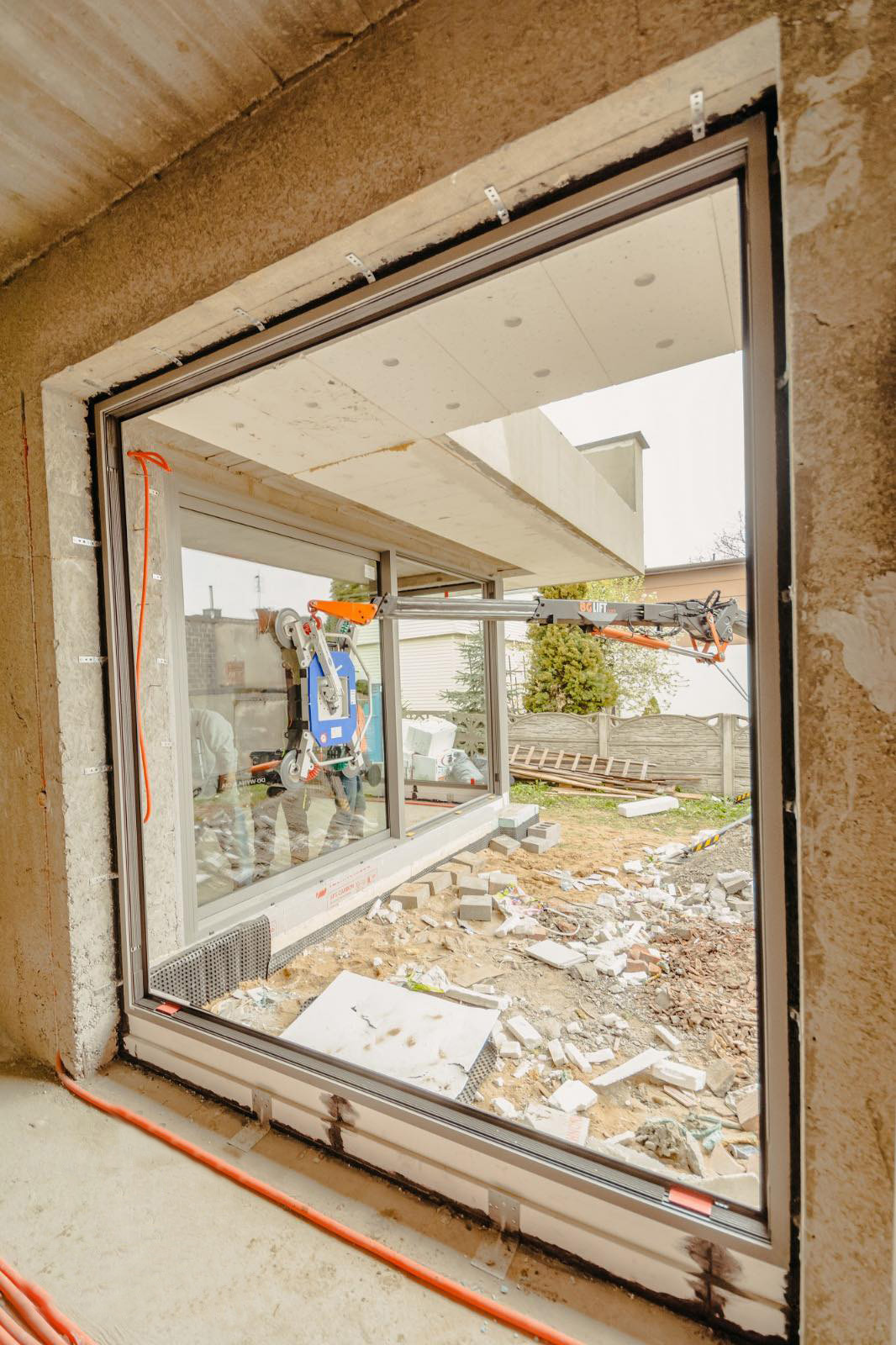 Montaż okna panoramicznego za pomocą specjalistycznego podnośnika próżniowego w surowym stanie budynku.