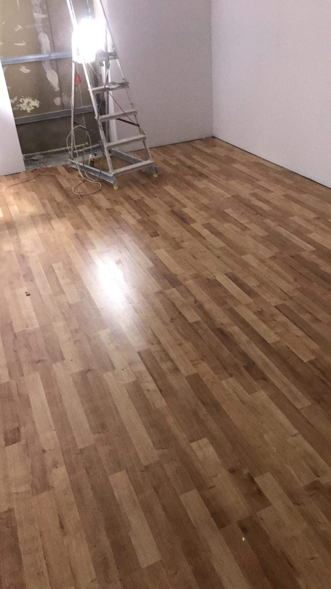 Nowa podłoga panelowa w pokoju, drabina oparta o ścianę w trakcie prac wykończeniowych, widoczny fragment ściany przed położeniem gładzi.
