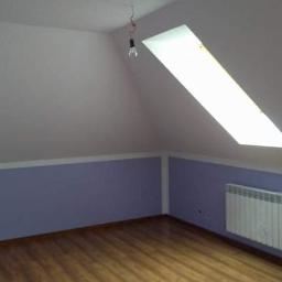 Usługi remontowo budowlane Paweł Magda - Pokój na poddaszu po remoncie: białe ściany, fioletowa lamperia, drewniana podłoga, okno dachowe i grzejnik. Wisząca żarówka bez klosza.