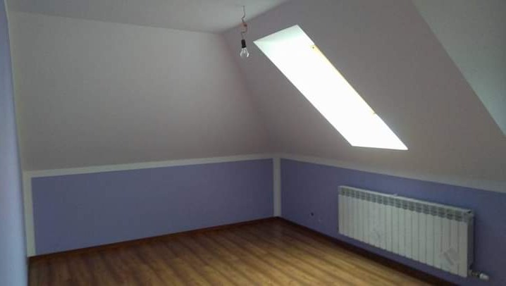 Pokój na poddaszu po remoncie: białe ściany, fioletowa lamperia, drewniana podłoga, okno dachowe i grzejnik. Wisząca żarówka bez klosza.