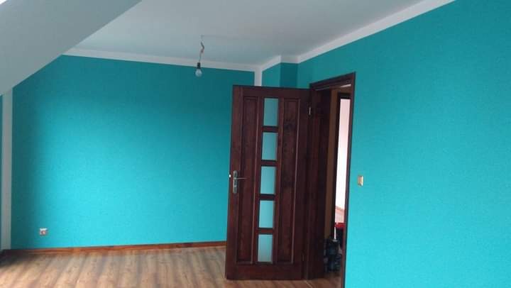 Pokój po odświeżeniu ścian w turkusowym odcieniu, z drewnianą podłogą i drzwiami z przeszkleniami, widoczna surowa żarówka.