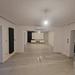 FIRMA HANDLOWO - USŁUGOWA Marcin Grabowski - Przestronne wnętrze w trakcie remontu, widoczne płytki podłogowe imitujące marmur, grzejnik panelowy na ścianie, białe ściany z widocznymi puszkami elektrycznymi, oraz system klimatyzacji pod sufitem.