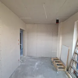 Pokój w trakcie remontu z zamontowanymi płytami kartonowo-gipsowymi na ścianach i suficie, widoczne kable elektryczne wystające ze ściany i sufitu, drabina oparta o ścianę.