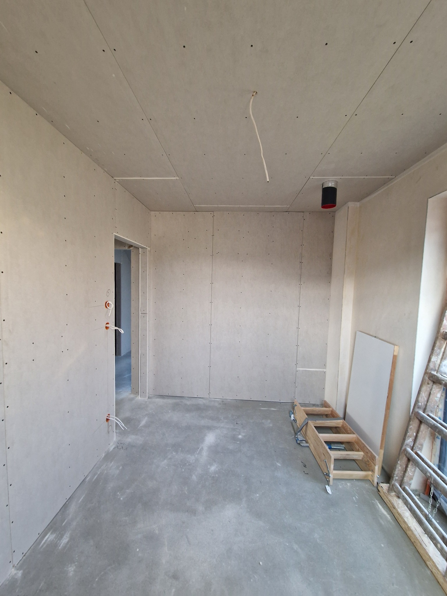 Pokój w trakcie remontu z zamontowanymi płytami kartonowo-gipsowymi na ścianach i suficie, widoczne kable elektryczne wystające ze ściany i sufitu, drabina oparta o ścianę.