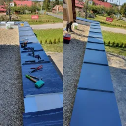 Widok z góry na blachę trapezową w kolorze granatowym, ułożoną na dachu podczas montażu, z widocznymi narzędziami dekarskimi, takimi jak młotki, nożyce do blachy, wkrętarka i skrzynka narzędziowa...