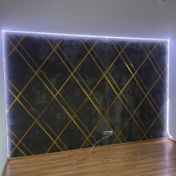 Usługi Remontowo Budowlane Sebastian Korczak - Ściana z dekoracyjnym tynkiem w odcieniach szarości, z geometrycznym wzorem ze złotych pasków i podświetleniem LED w Radomiu.