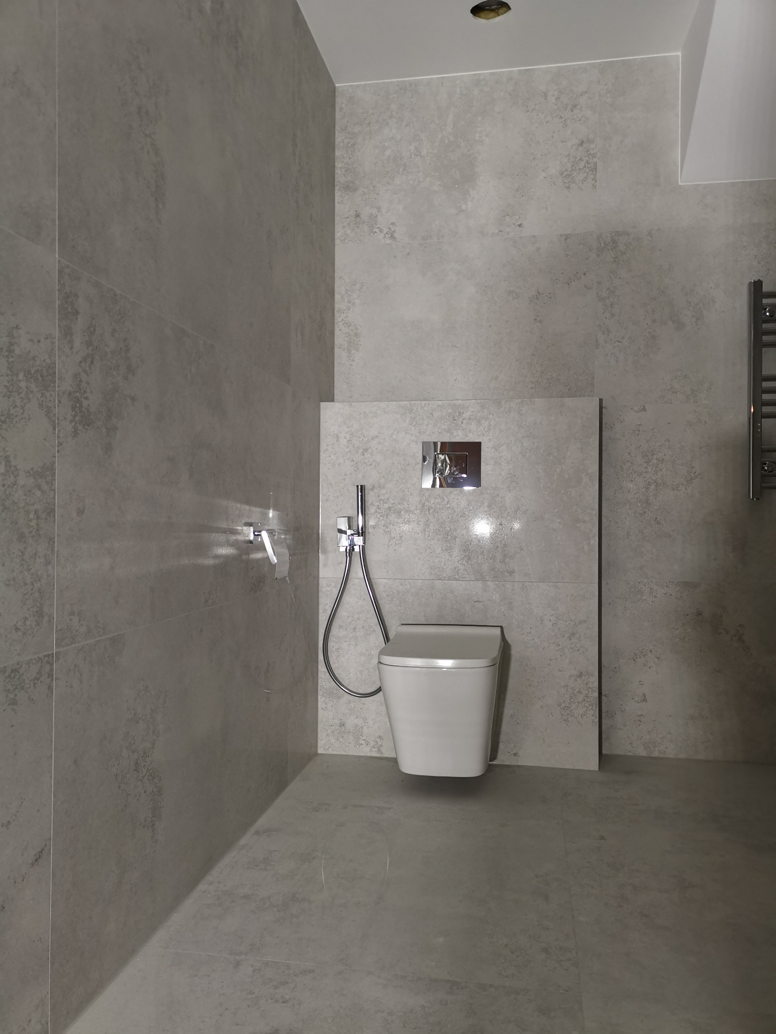 Nowoczesna toaleta podwieszana z chromowaną armaturą i szarą, teksturowaną okładziną ścienną w minimalistycznej łazience.