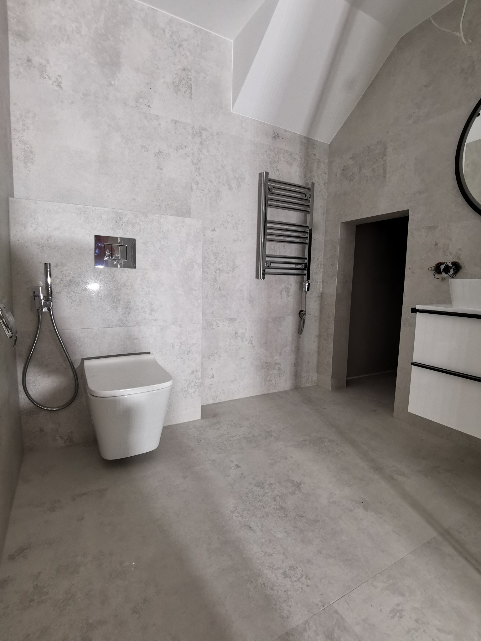 Nowoczesna łazienka w odcieniach szarości z podwieszaną toaletą, grzejnikiem drabinkowym i umywalką z szafką w minimalistycznym stylu, wykończona płytkami imitującymi beton.