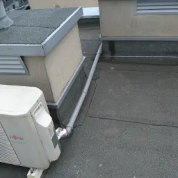 Jednostka zewnętrzna klimatyzacji Fujitsu DC Inverter zamontowana na płaskim dachu, z widocznym odprowadzeniem skroplin rurą PCV i izolacją termiczną na łączeniu.