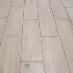 Ułożona podłużnie jasna podłoga z płytek imitujących drewno, z widocznymi fugami w odcieniach szarości.