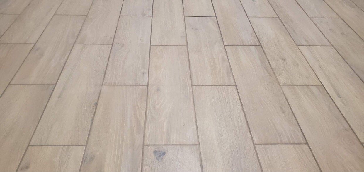 Ułożona podłużnie jasna podłoga z płytek imitujących drewno, z widocznymi fugami w odcieniach szarości.