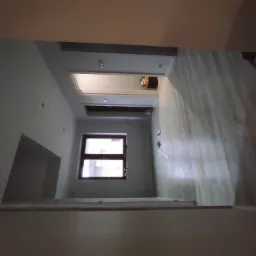 Wnętrze w trakcie remontu: widok na pokój z oknem i wykończoną podłogą, ściany przygotowane do dalszych prac.