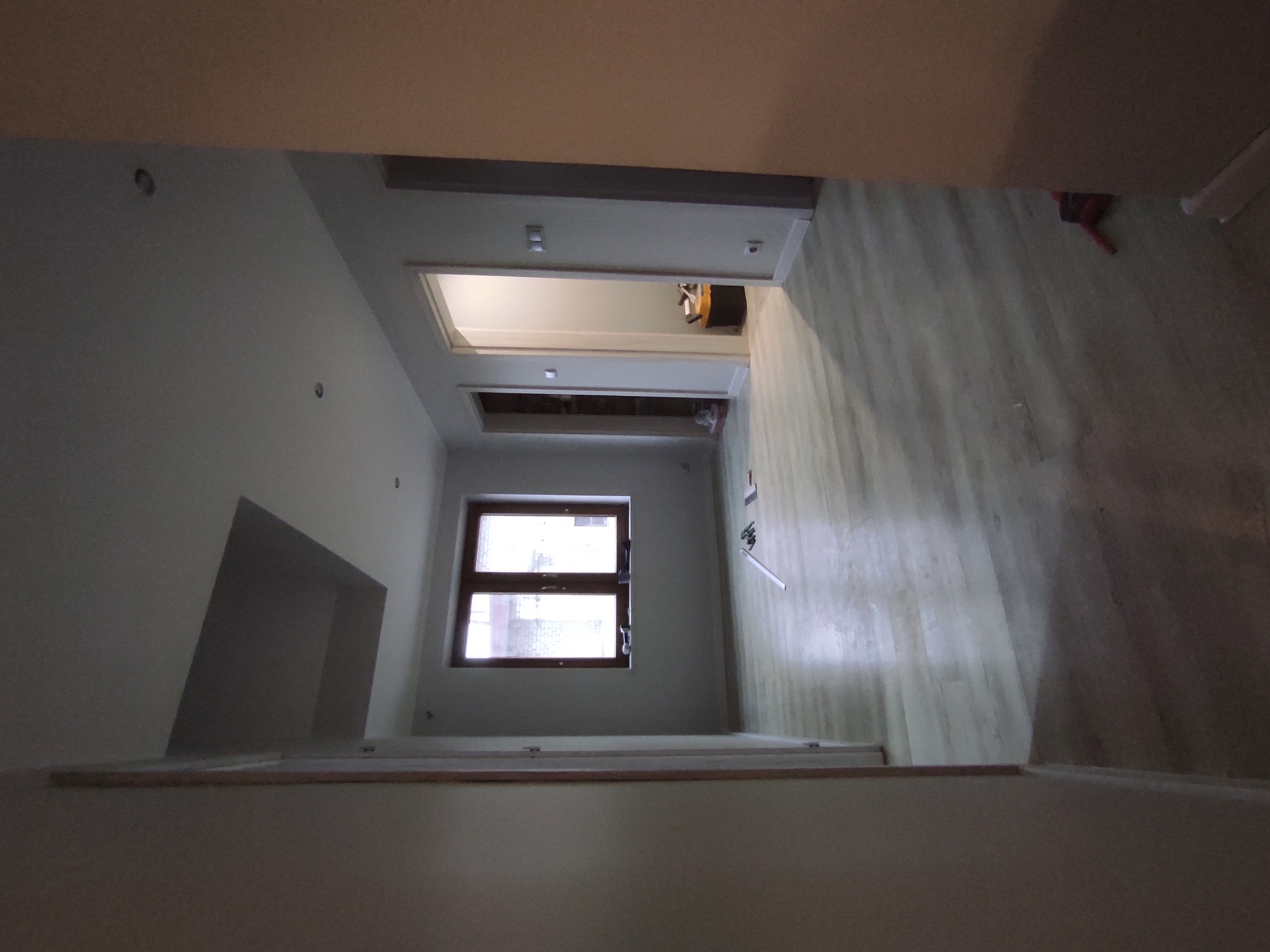 Wnętrze w trakcie remontu: widok na pokój z oknem i wykończoną podłogą, ściany przygotowane do dalszych prac.