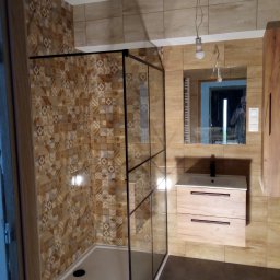 Roberto bud - Nowoczesna kabina prysznicowa z czarnymi profilami, wzorzyste płytki ścienne w odcieniach brązu, umywalka z drewnopodobną szafką, lustro z odbiciem osoby robiącej zdjęcie, sufit z niedokończonym...