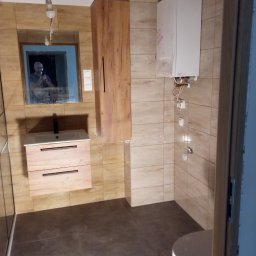 Roberto bud - Łazienka z beżowymi płytkami, wiszącą szafką z umywalką z drewnianymi frontami, białym bojlerem i lustrem, w którym odbija się osoba robiąca zdjęcie.