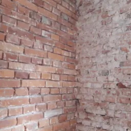 Narożnik ściany z czerwonej cegły z fragmentami starej farby, ukazujący stan przed remontem lub podczas prac murarskich.