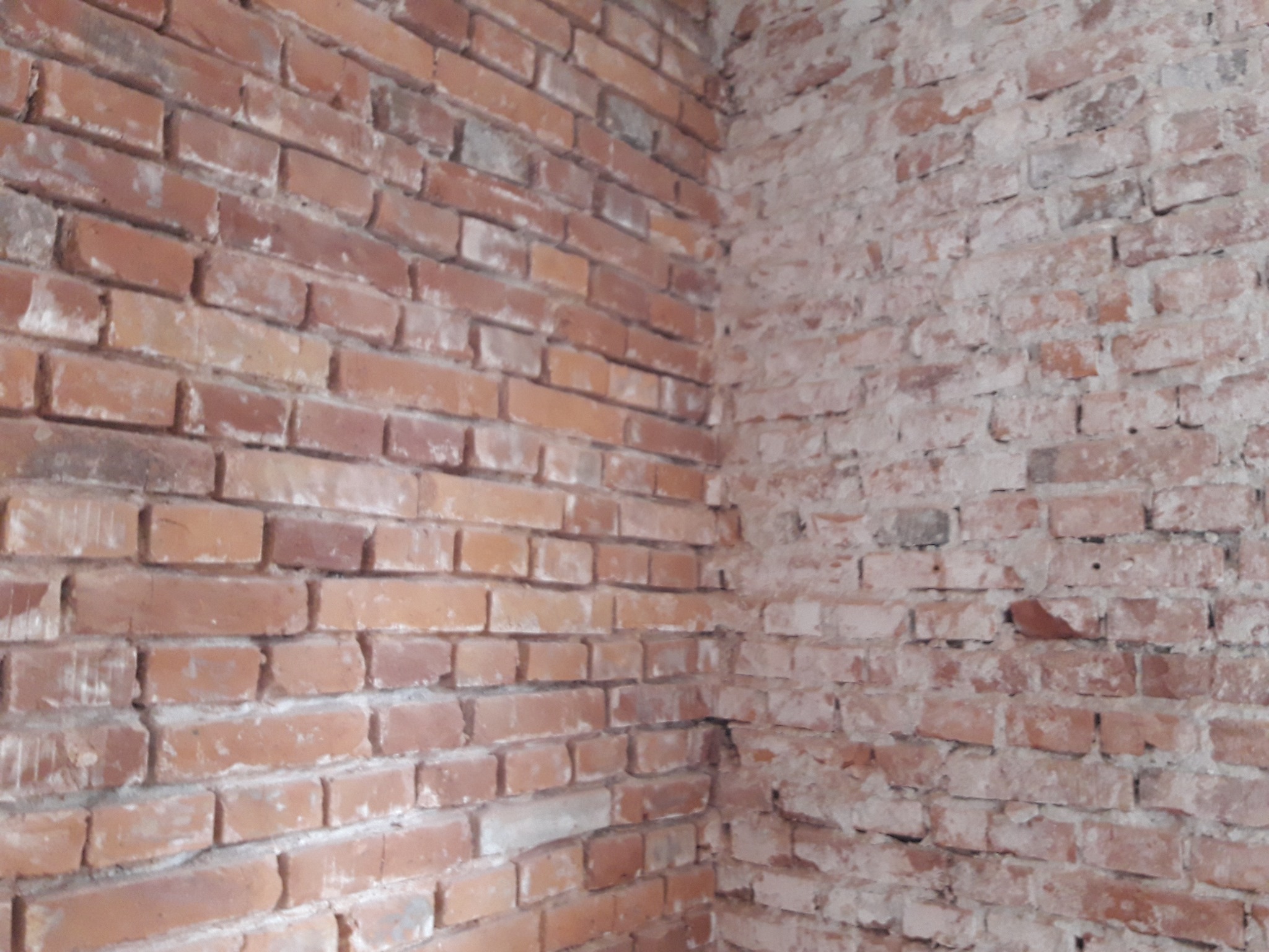 Narożnik ściany z czerwonej cegły z fragmentami starej farby, ukazujący stan przed remontem lub podczas prac murarskich.