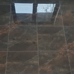 Grzegorz Mazur - Błyszczące, ciemne płytki podłogowe z marmurkowym wzorem, odbijające światło z okna dachowego.