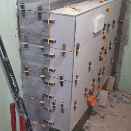 Grzegorz Mazur - Proces układania szarych i białych płytek ceramicznych na ścianie, z użyciem klipsów poziomujących i poziomicy PRO, widoczne fragmenty instalacji hydraulicznej