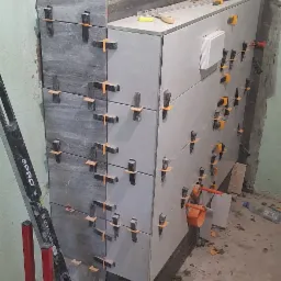 Proces układania szarych i białych płytek ceramicznych na ścianie, z użyciem klipsów poziomujących i poziomicy PRO, widoczne fragmenty instalacji hydraulicznej