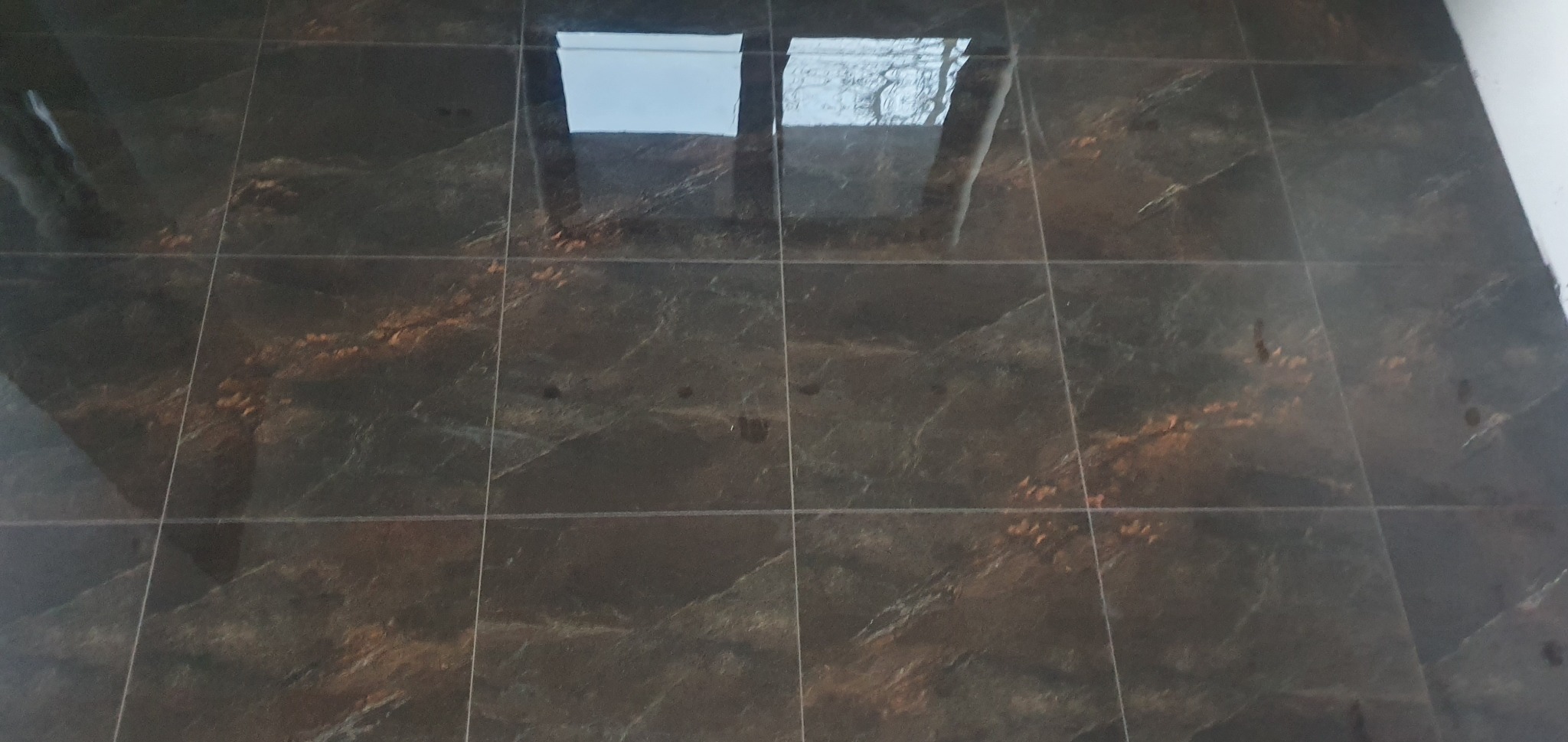 Błyszczące, ciemne płytki podłogowe z marmurkowym wzorem, odbijające światło z okna dachowego.