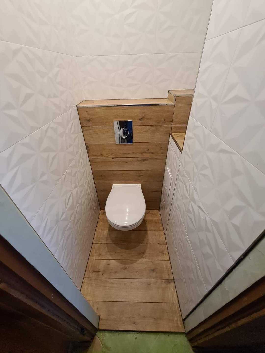 Wykończona łazienka w Przyłęku z podwieszaną toaletą, drewnopodobną podłogą i ścianą z drewnianą zabudową oraz białymi trójwymiarowymi płytkami na pozostałych ścianach.