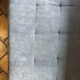 Szary materac z guzikami na brązowej podłodze z płytek, widok z góry