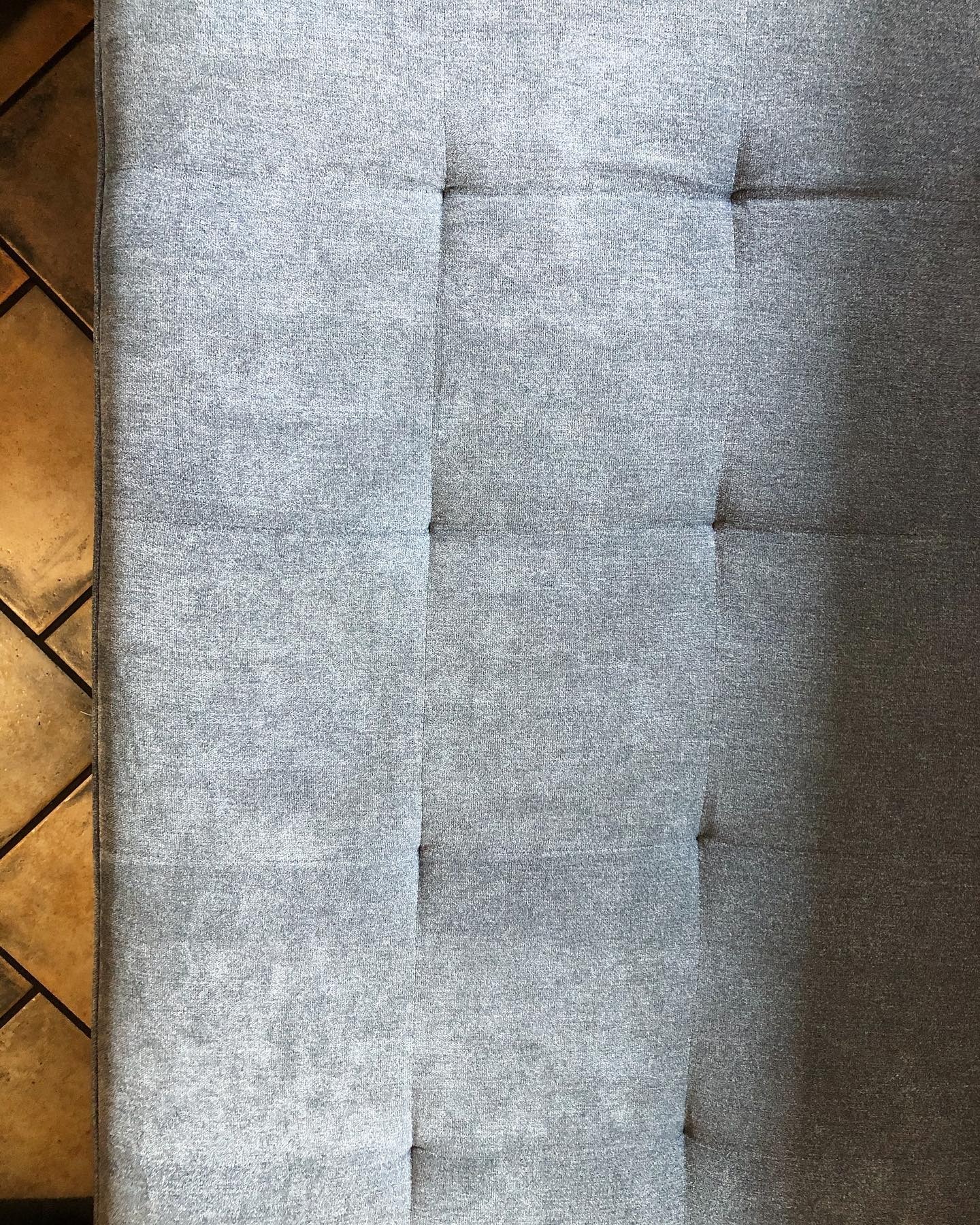 Szary materac z guzikami na brązowej podłodze z płytek, widok z góry