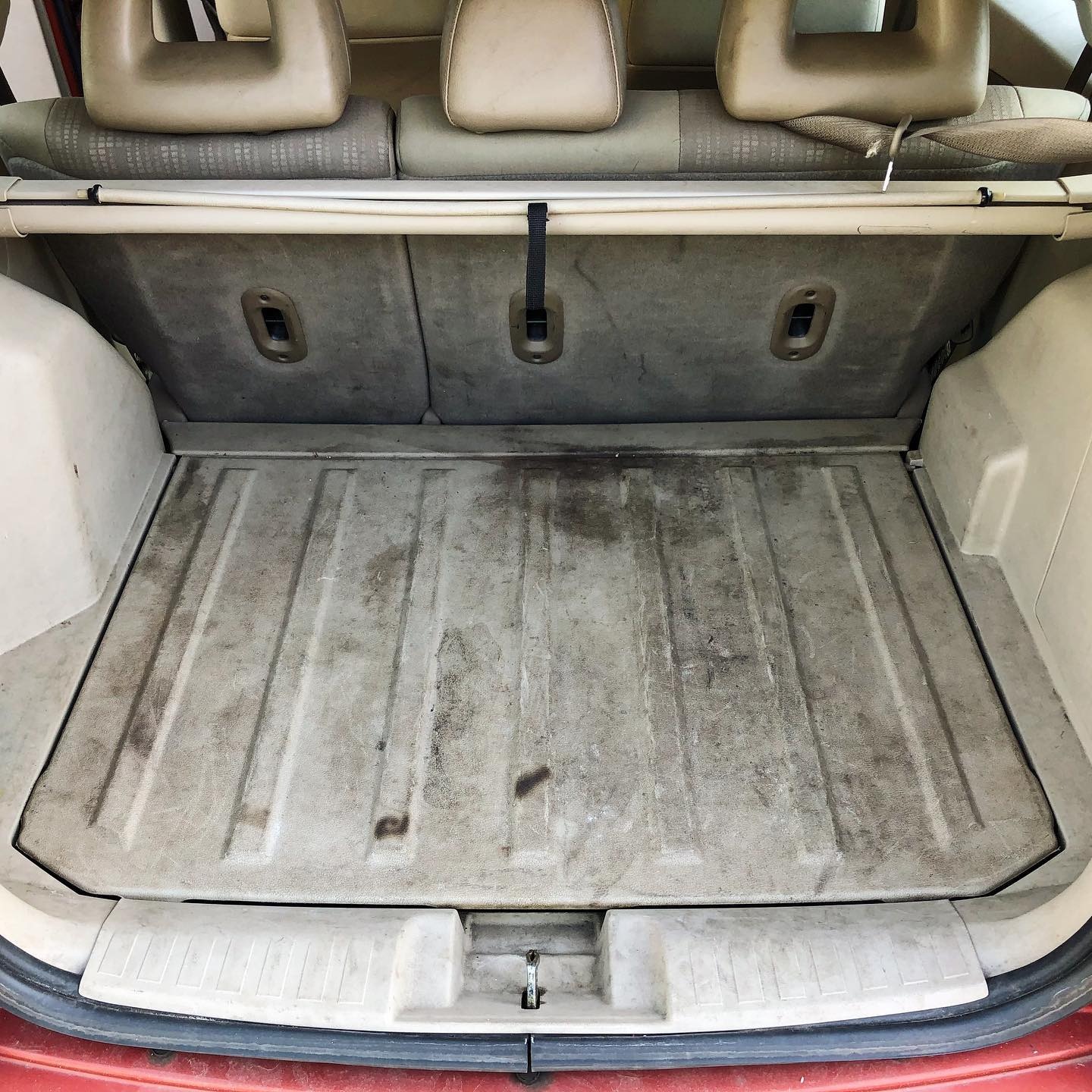 Brudny bagażnik samochodu z beżową tapicerką i widocznymi plamami na podłodze, przed czyszczeniem.
