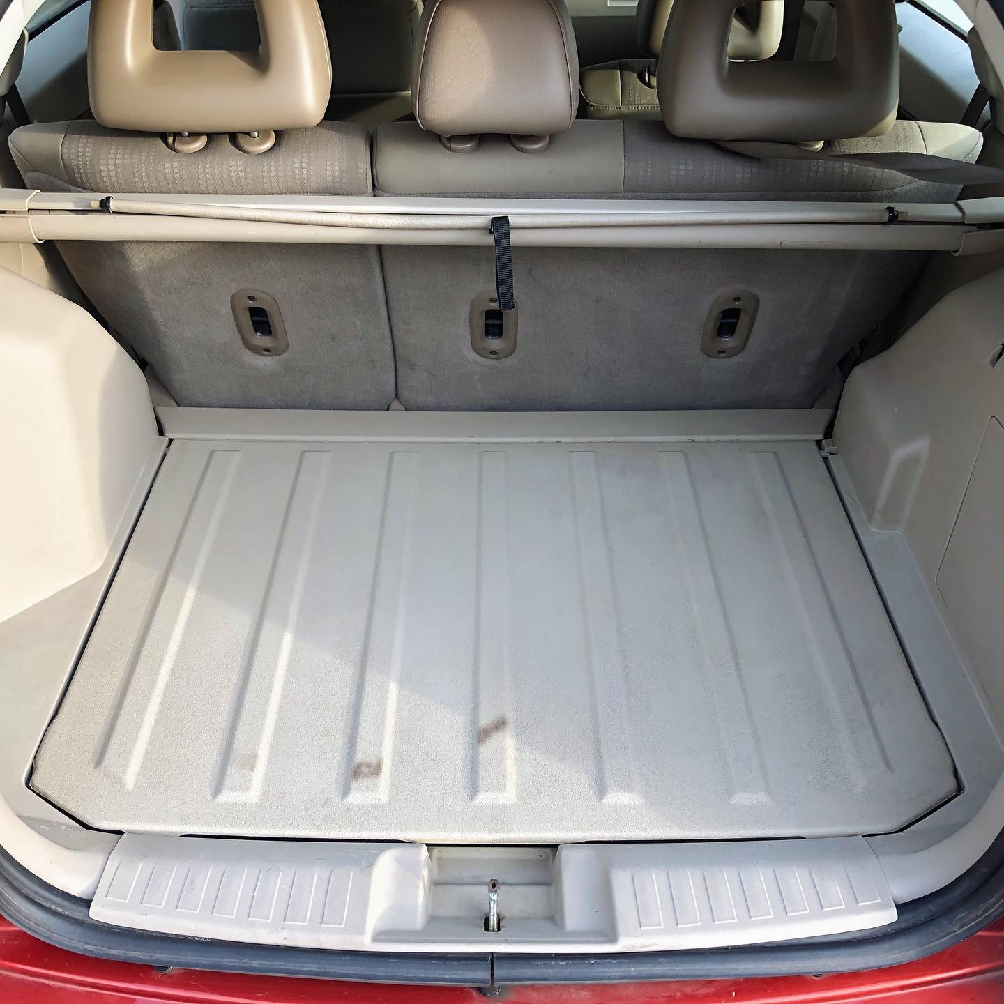 Czysty bagażnik samochodu typu hatchback z beżową plastikową wykładziną i widocznymi zagłówkami tylnych siedzeń.