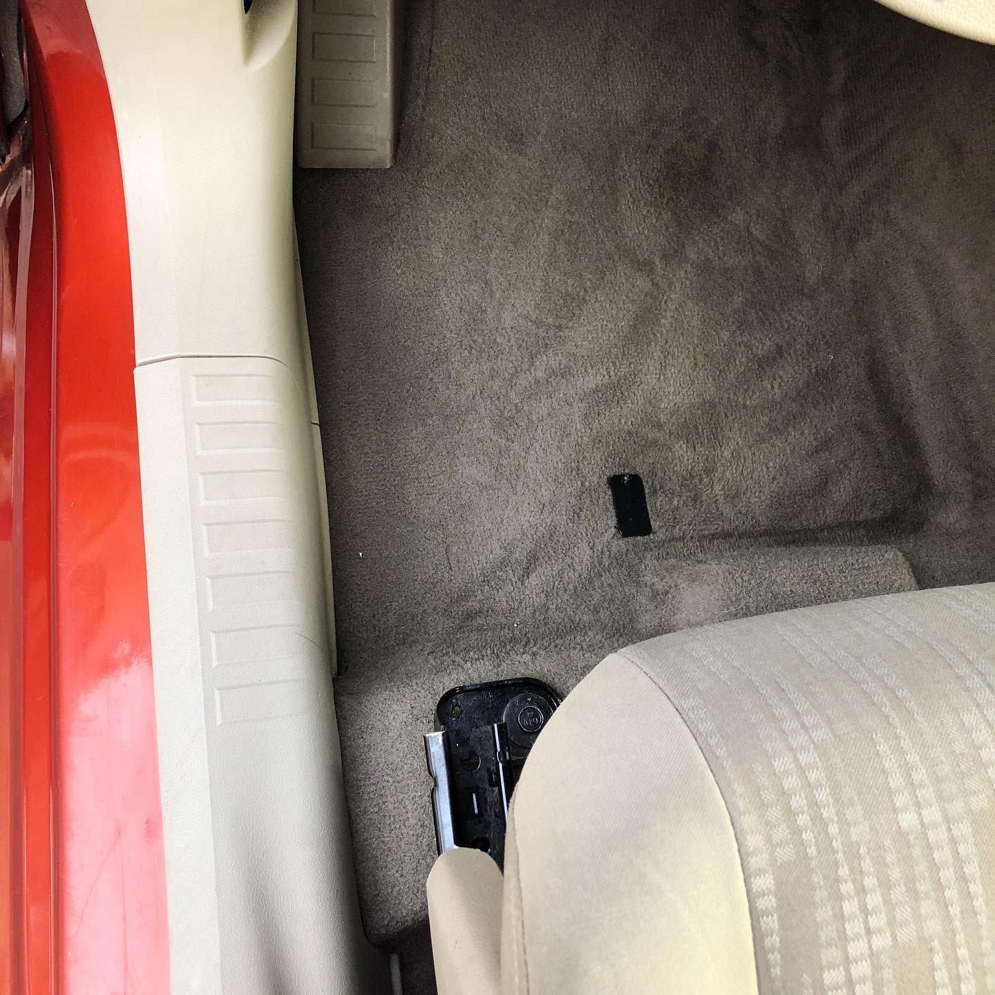 Wnętrze samochodu z widoczną brudną, szarą wykładziną podłogową, jasnym fotelem i fragmentem czerwonej karoserii.