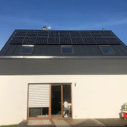 Nowoczesny dom jednorodzinny z panelami fotowoltaicznymi na dachu, widoczne okna dachowe i zabawka ogrodowa na tarasie.