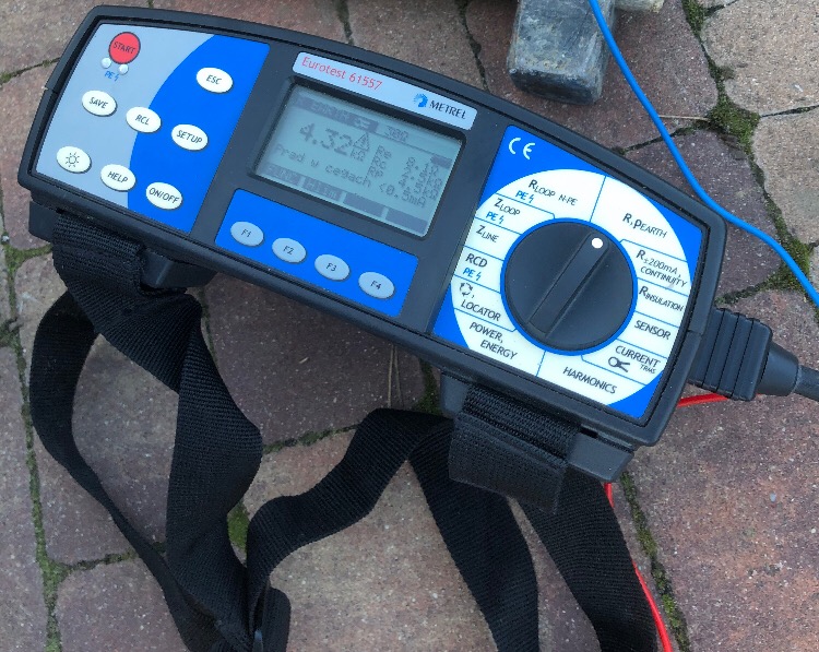 Miernik Eurotest 61557 firmy Metrel, leżący na brukowanej powierzchni, wyświetlający wynik pomiaru 4.32 kΩ, z widocznymi przewodami pomiarowymi i paskiem do przenoszenia.