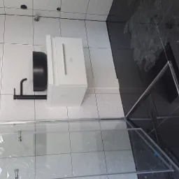 Nowoczesna łazienka z biało-czarną kolorystyką, kabiną prysznicową ze szklanymi drzwiami, umywalką nablatową w kolorze czarnym, białą szafką pod umywalką oraz lustrem z podświetleniem LED.