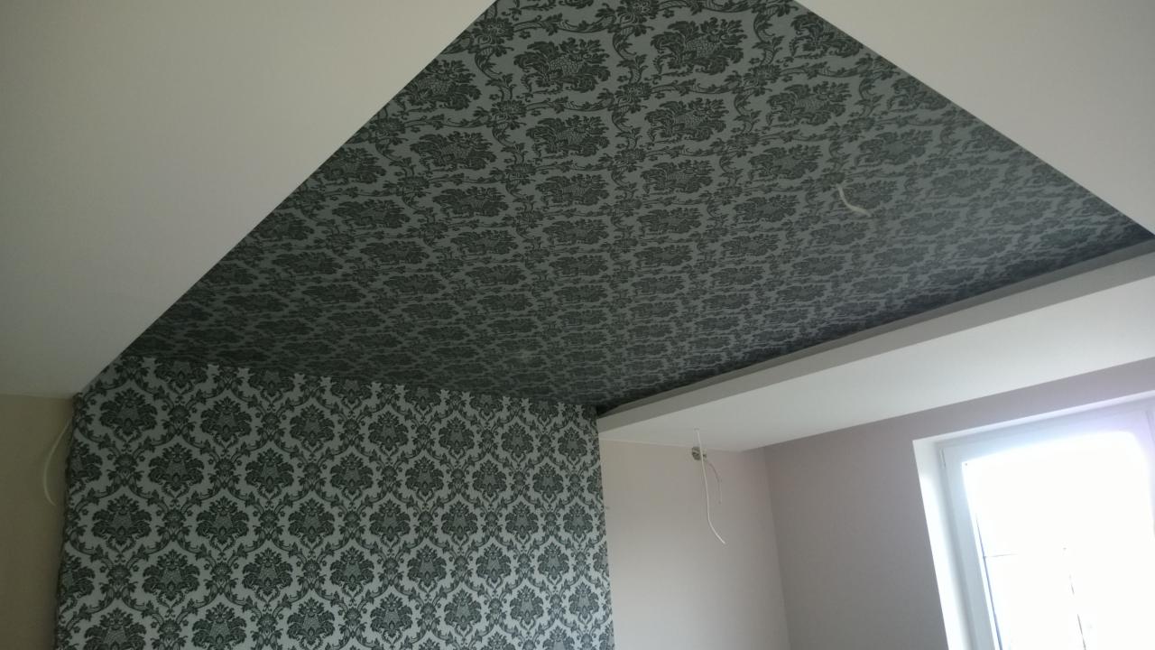 Pokój po remoncie: wzorzysta tapeta na ścianie i skośnym suficie, białe listwy przysufitowe, fragment okna. Wykończenie wnętrza w klasycznym stylu.