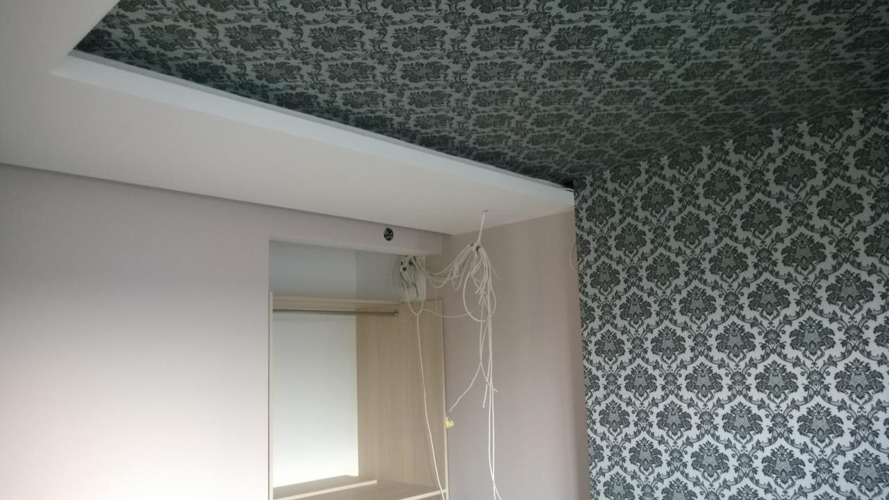 Wykończone wnętrze z dekoracyjną tapetą na suficie i ścianie, zabudowa garderoby z widocznymi kablami oświetleniowymi. Częściowo gotowe pomieszczenie.