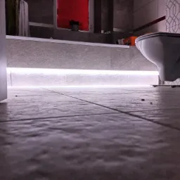 Podświetlenie LED pod wanną w łazience w Gnieźnie, widok z poziomu podłogi, na ścianie wzorzyste płytki i wisząca toaleta.