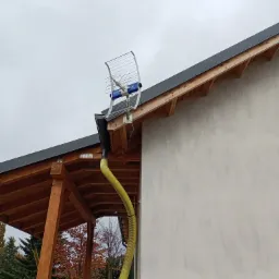 Antena telewizyjna zamontowana na dachu domu jednorodzinnego z nową elewacją, widoczna żółta rura spustowa, dach z drewnianą konstrukcją i szarą blachą.