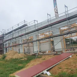 Budowa domu z prefabrykatów: ściany modułowe, rusztowania i dźwig w tle, widoczne elementy konstrukcyjne.