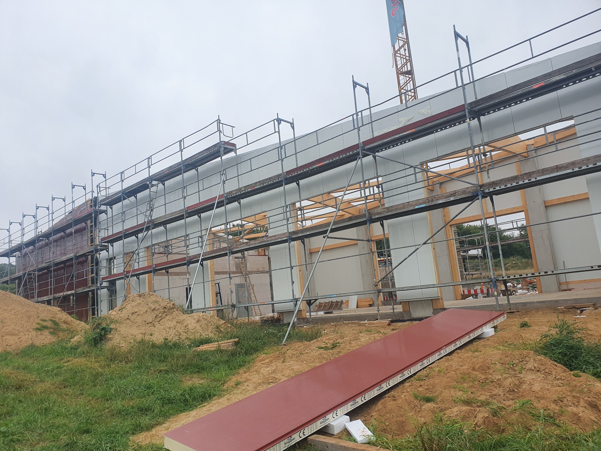 Budowa domu z prefabrykatów: ściany modułowe, rusztowania i dźwig w tle, widoczne elementy konstrukcyjne.