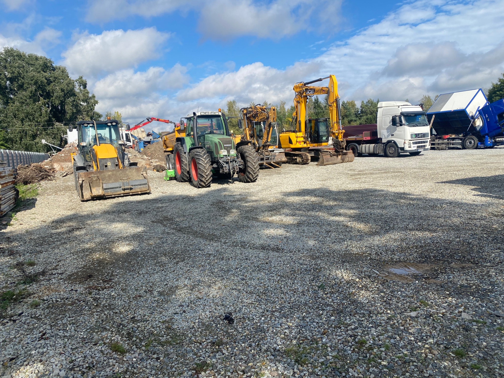 Sprzęt budowlany (koparki, ciągnik, wywrotki) na placu w Wrocławiu. Widoczne pozostałości po rozbiórce i gruz, co sugeruje prace ziemne i przygotowanie terenu.