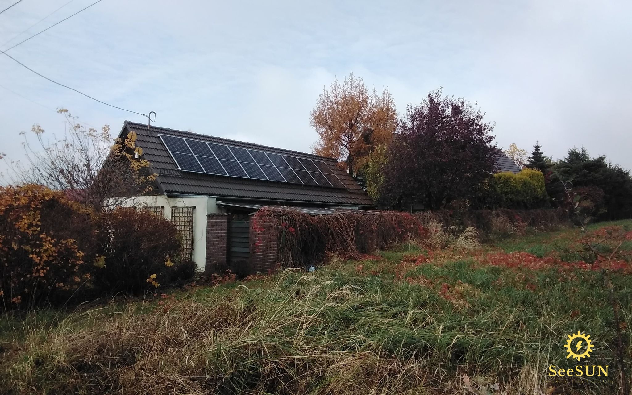 Dom z brązową dachówką i panelami słonecznymi, otoczony jesienną roślinnością w Jasienicy.